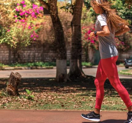 A woman jogs on a path surrounded by trees and vibrant flowers, embodying a healthy lifestyle.