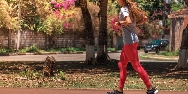 A woman jogs on a path surrounded by trees and vibrant flowers, embodying a healthy lifestyle.